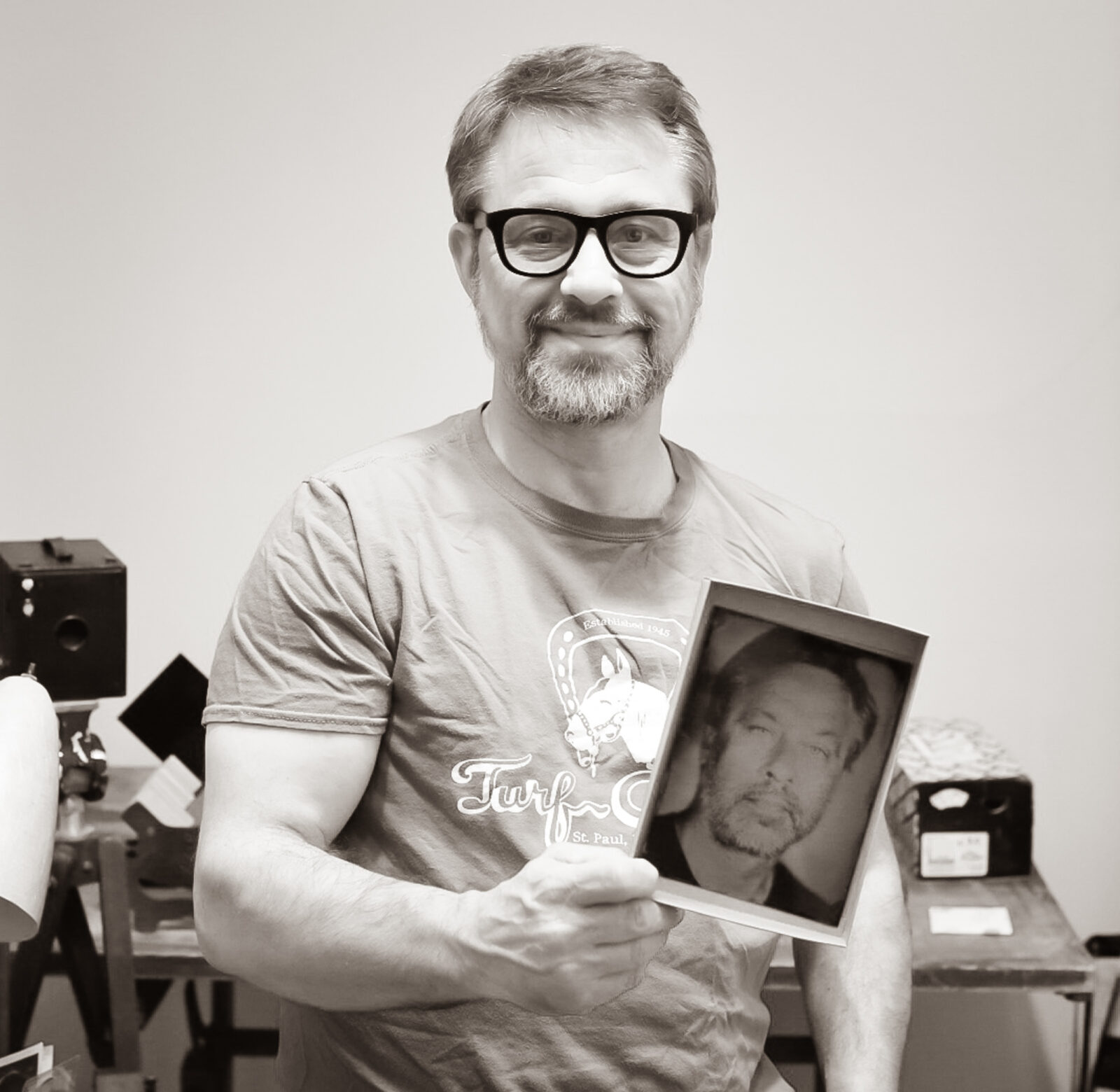 Man looking in the camera holding a tintype photograph of himself