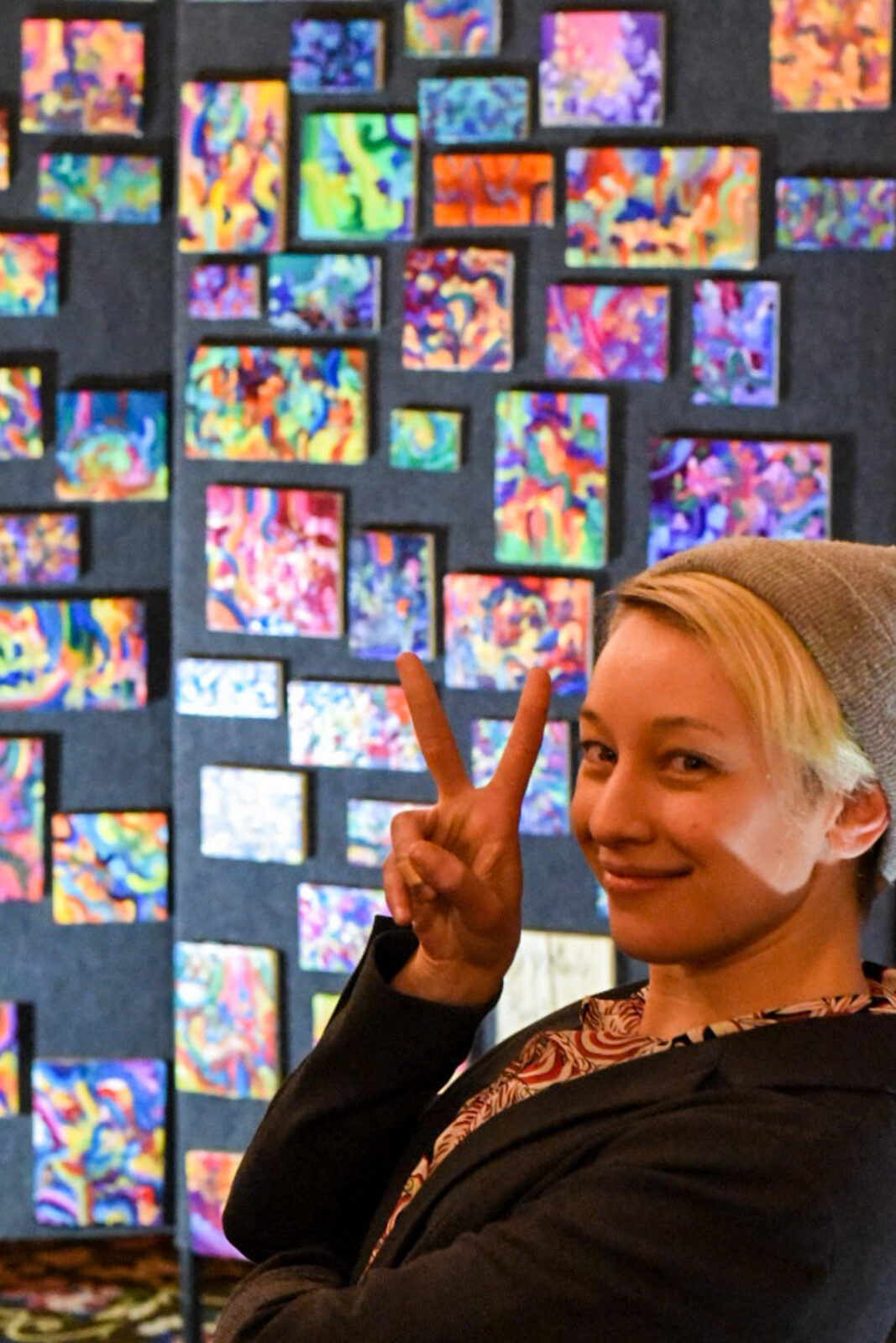 Person posing holding up a peace sign standing in front of a display of artwork