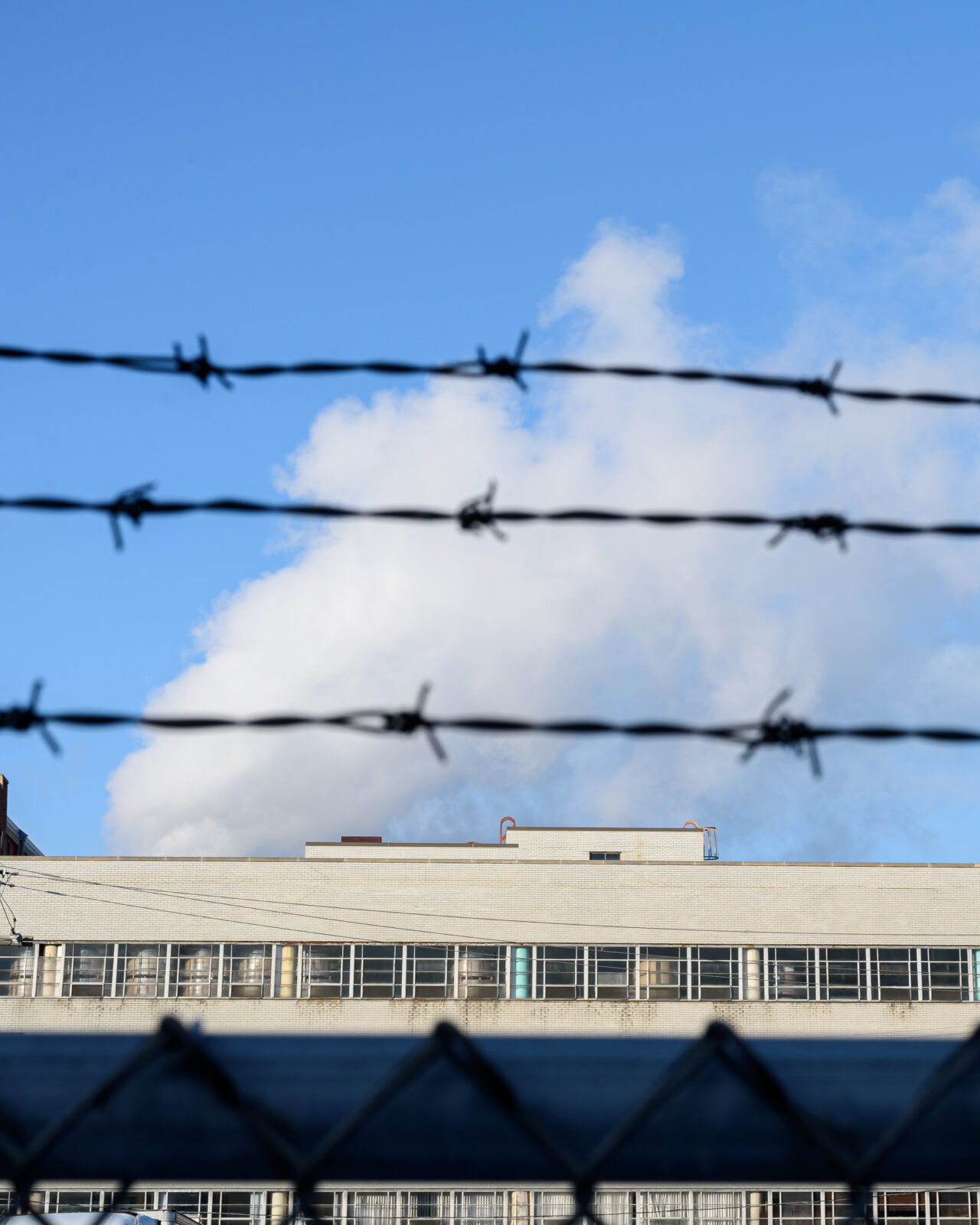 blue sky with fluffy cloud over a building roof behind chain link fence
