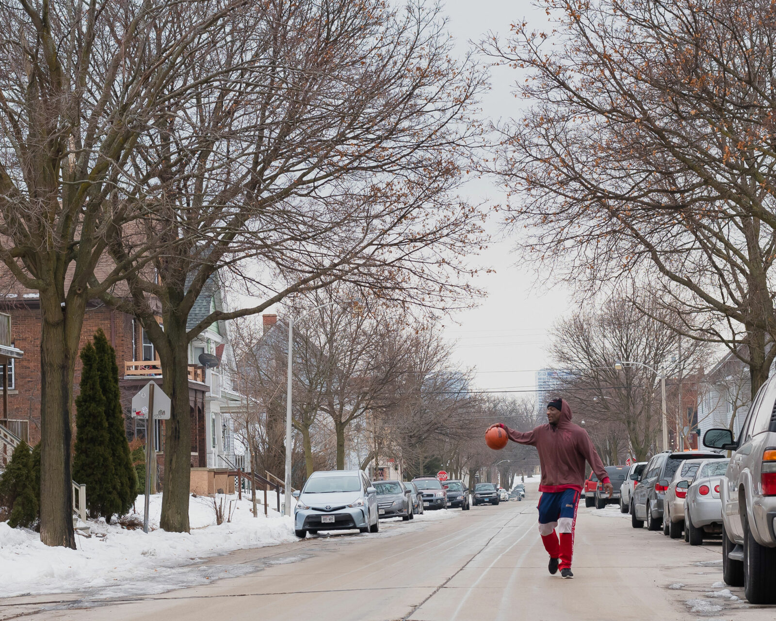 a man in the middle of a neighborhood street with a basketball