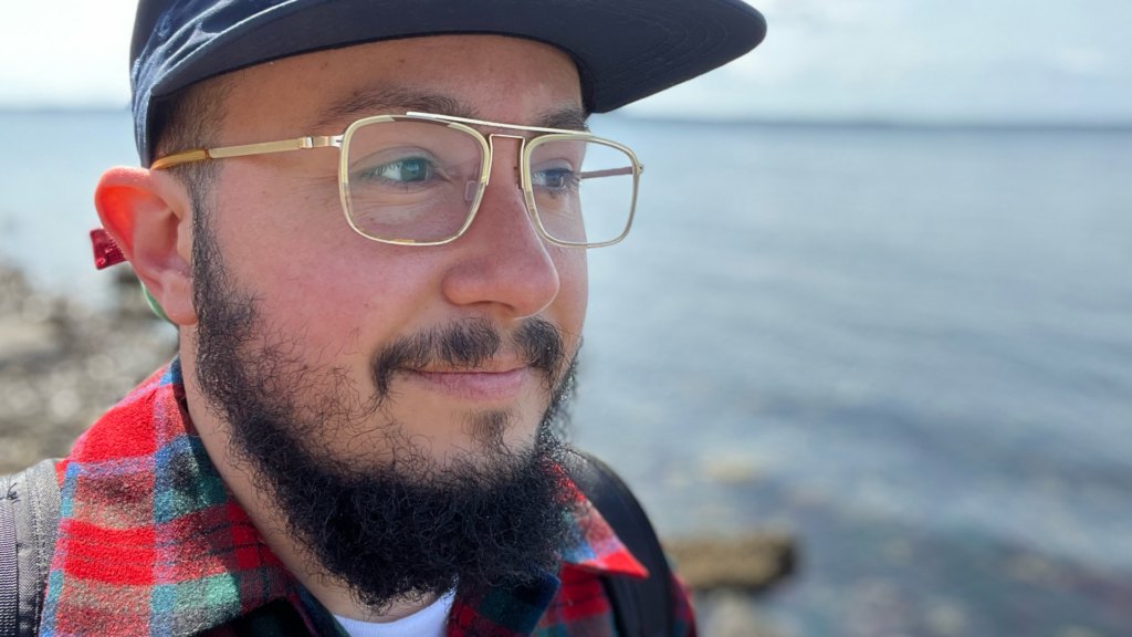 Close-up shot, exterior, body of water in the background, Olive Baez Bendorf looking off camera with a slight smile