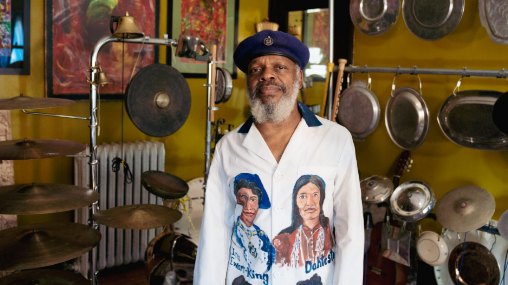 Photo of Douglas Ewart with his studio behind him showing musical instruments.