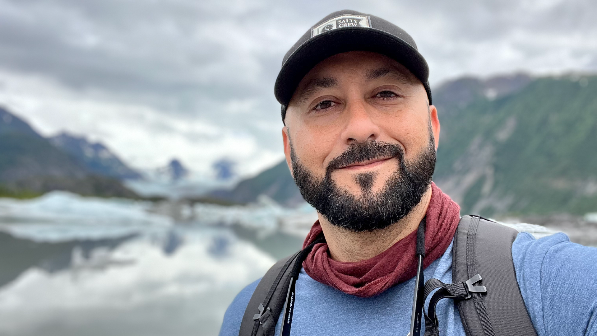 Craig Santos Perez author portrait, exterior, close-up, water, mountains, and sky in the background.